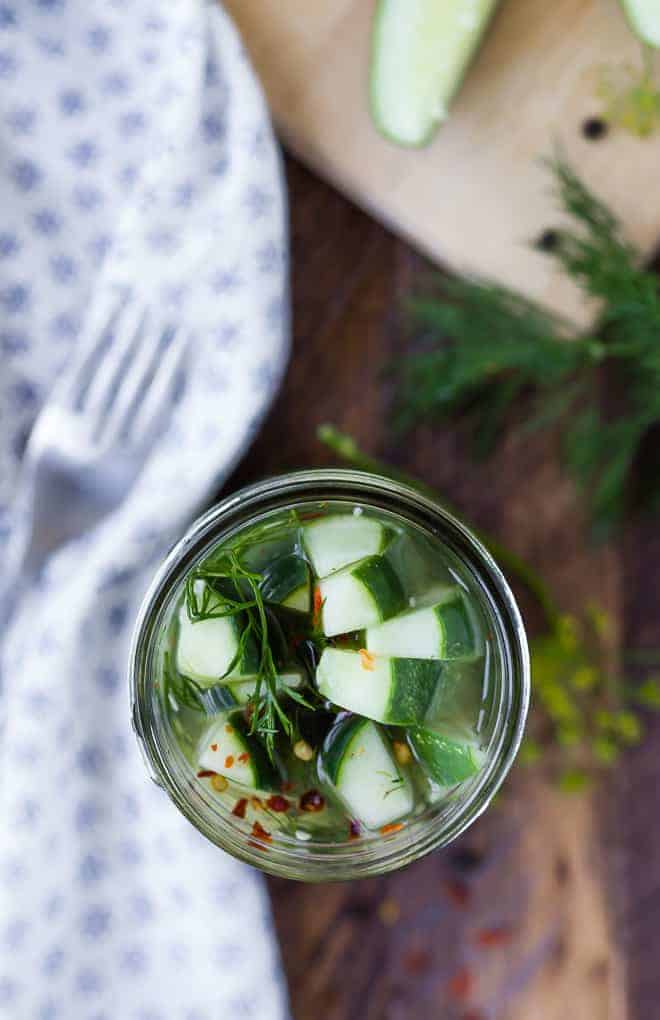 Overhead image of dill pickle spears in a jar. Dill, red pepper flakes, and peppercorns are also in the photo. 