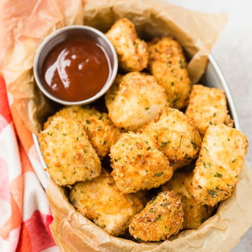 Image of air fryer chicken nuggets in a basket, shot from above. BBQ sauce also pictured.