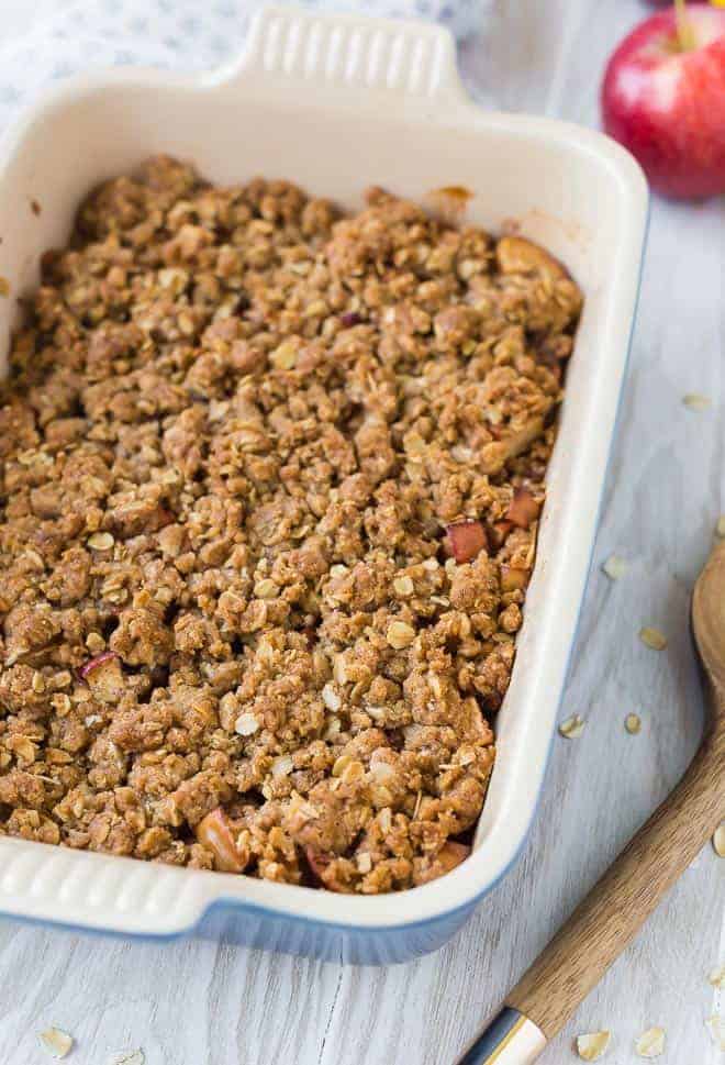 Overhead view of apple crisp in a ceramic baking dish next to a wooden spoon.