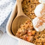 Close up of a spoon stuck into the corner of apple crisp topped with scoops of ice cream and cinnamon.