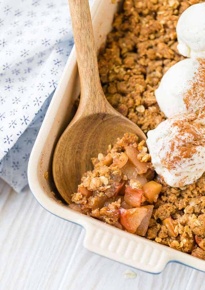 Close up of a spoon stuck into the corner of apple crisp topped with scoops of ice cream and cinnamon.