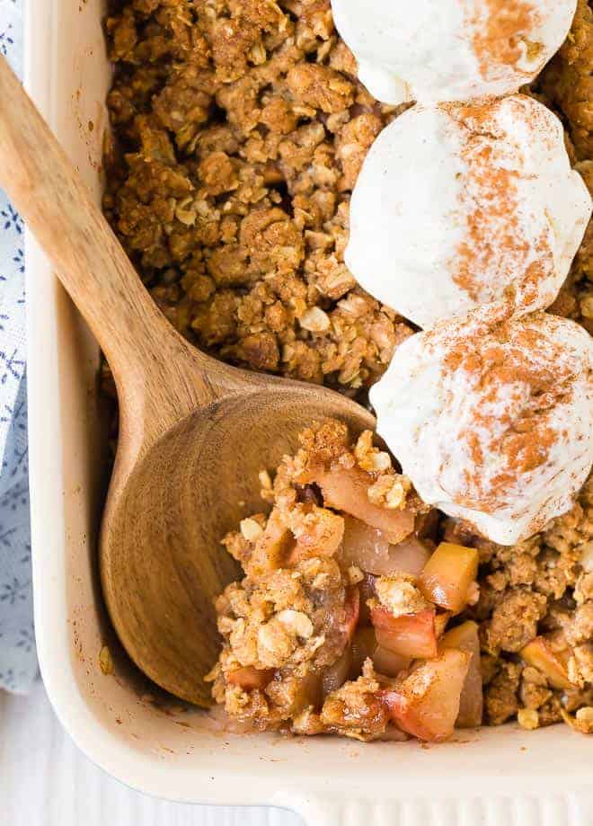 Close up of a spoon stuck into the corner of apple crisp topped with scoops of ice cream and cinnamon.