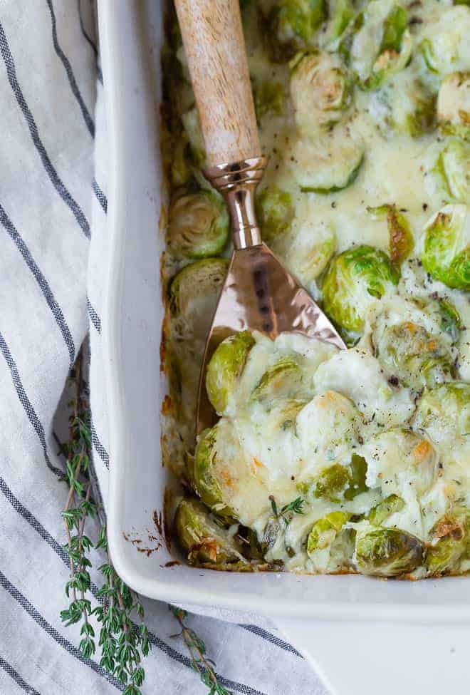 Close up view of Brussels sprouts and cheese in a white baking dish.