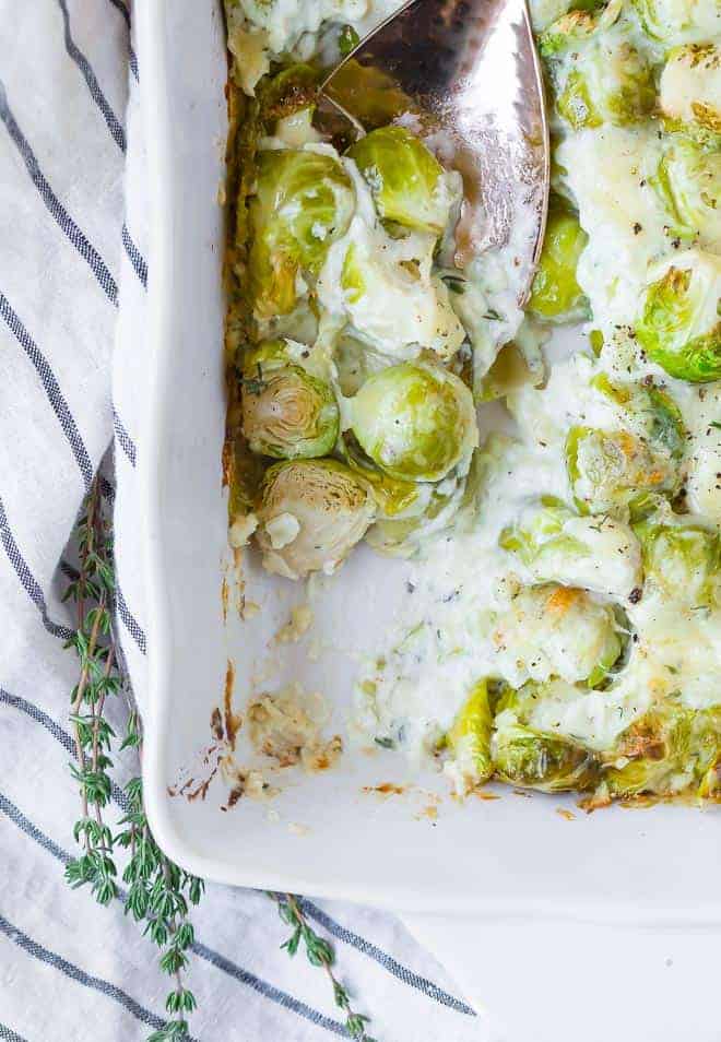 Cheesy brussels gratin being scooped out a white baking dish.