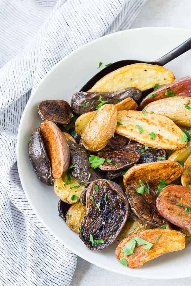 Image of fingerling potatoes in a white bowl. Chopped fresh parsley is sprinkled on top.