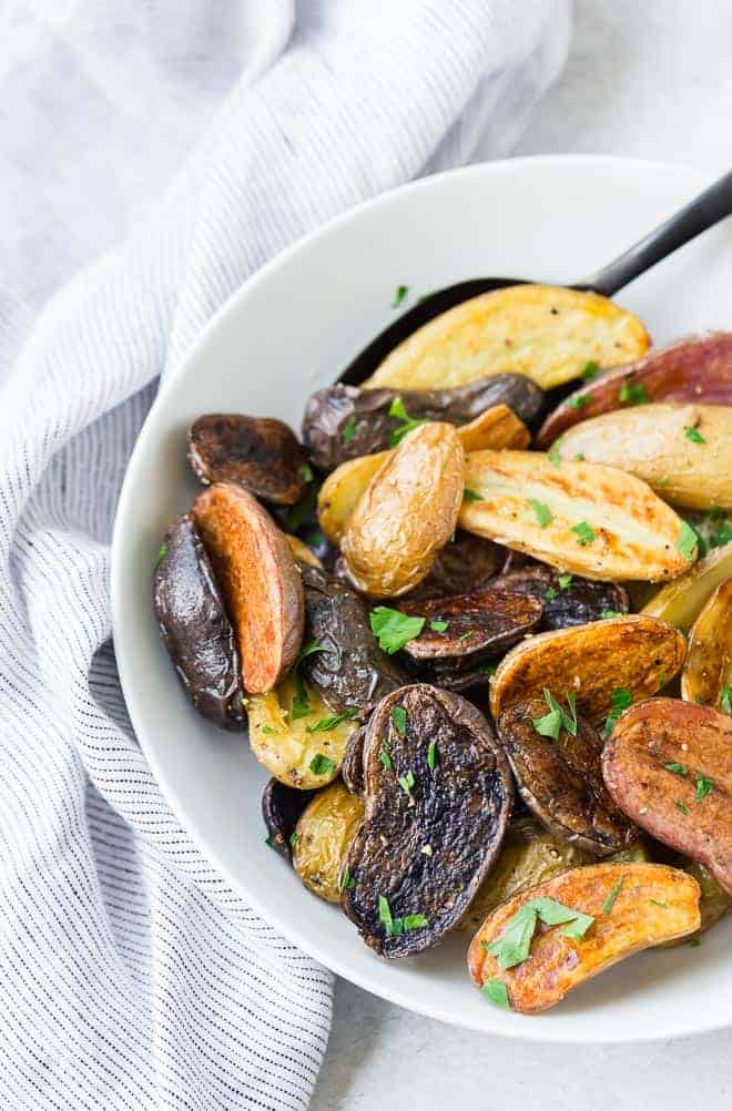 Image of beautiful colorful fingerling potatoes in a white bowl with a black spoon.