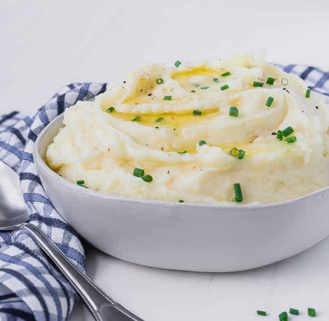 Creamy mashed potatoes in a bowl topped with melting butter and chives. Blue and white linen in background.