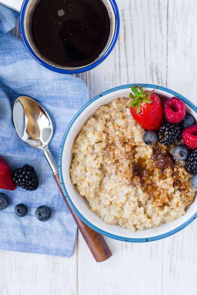 Photograph of pressure cooker steel coat oats, topped with berries. A spoon and a cup of coffee are also pictured.