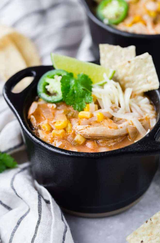 Serving of white chicken chili in small black crock, garnished with tortilla chips and other toppings.