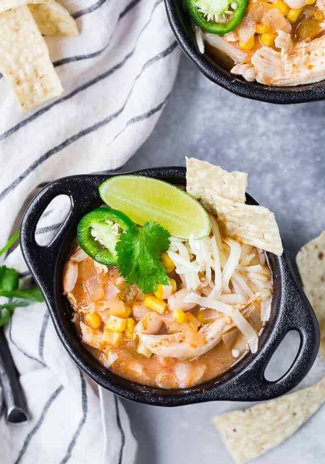 Image of Instant Pot White Chicken Chili in a black bowl with two handles. White chili is garnished with lime, cilantro, jalapeno and tortilla strips. 