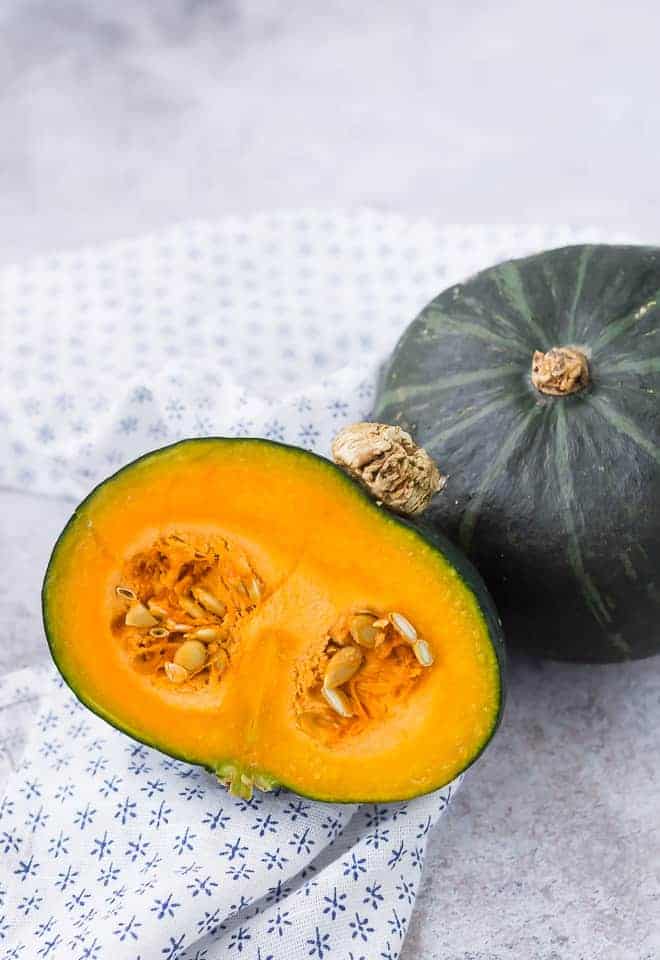 Image of a whole kabocha squash and a half kabocha squash with the seeds still present.