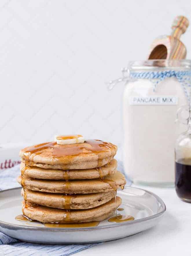 A stack of pancakes on a plate, topped with a pat of butter and lots of maple syrup.