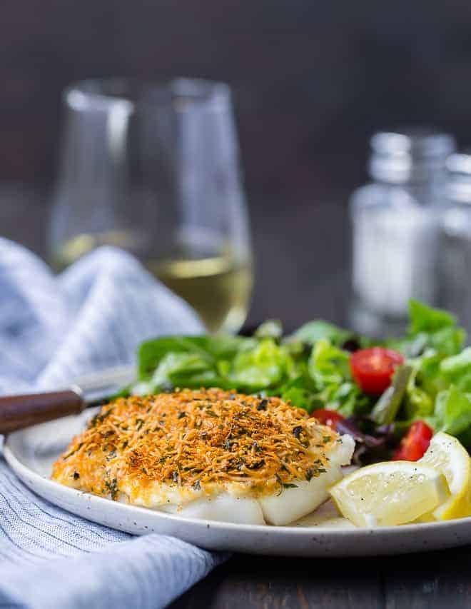 Image of baked parmesan cod with a glass of wine in the background.