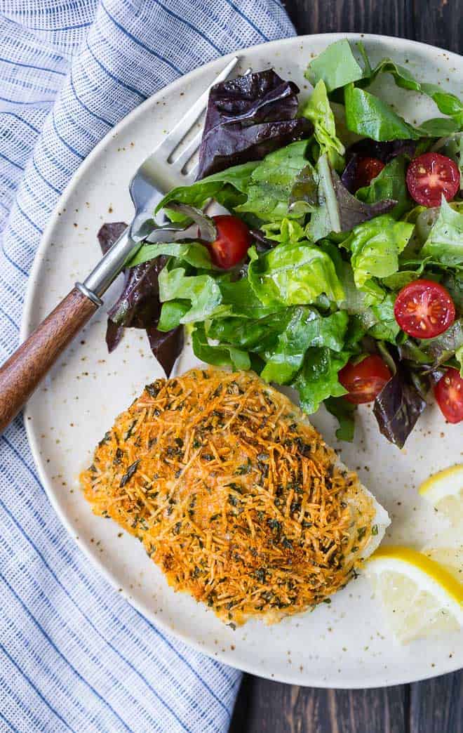 Image of baked cod with a parmesan crust. Served on a plate with a tossed salad.