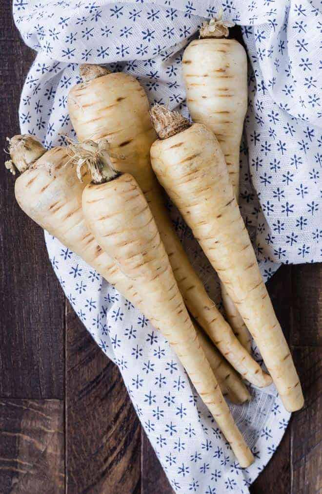 Image of 5 raw, unpeeled parsnips on blue print cloth.