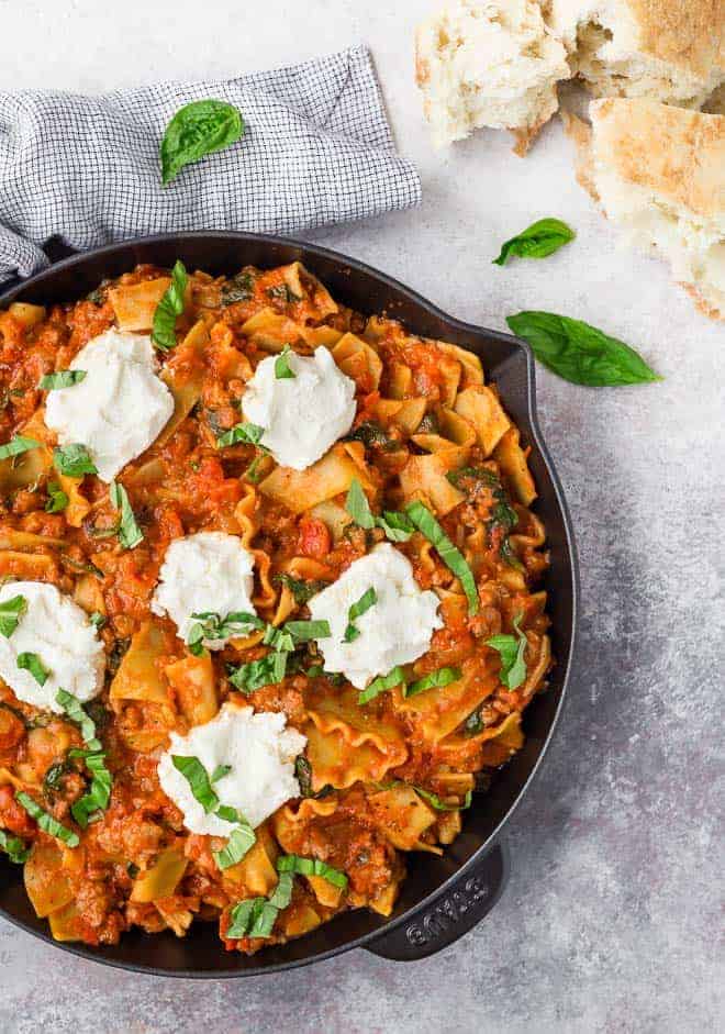 Image of skillet lasagna in a black cast iron pan. Ricotta is spooned on top.