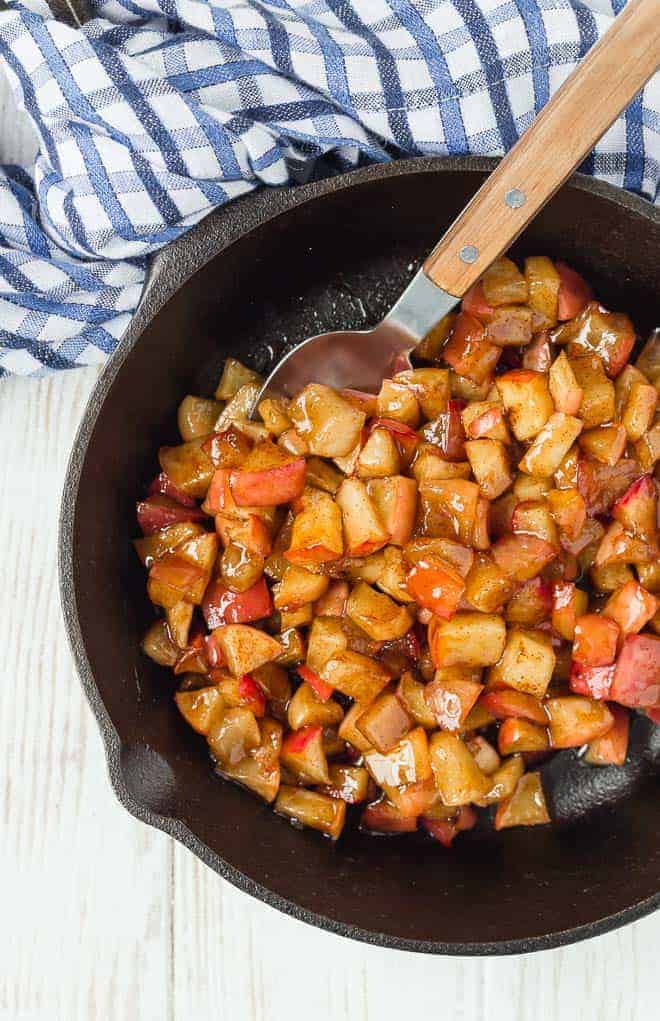 Apple cinnamon compote in a cast iron skillet, with a spoon. 