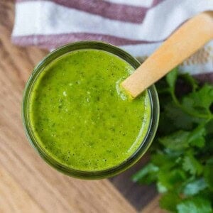 Image of a jar of freshly homemade salsa verde, shot from above. A wooden spoon is in the jar as well.