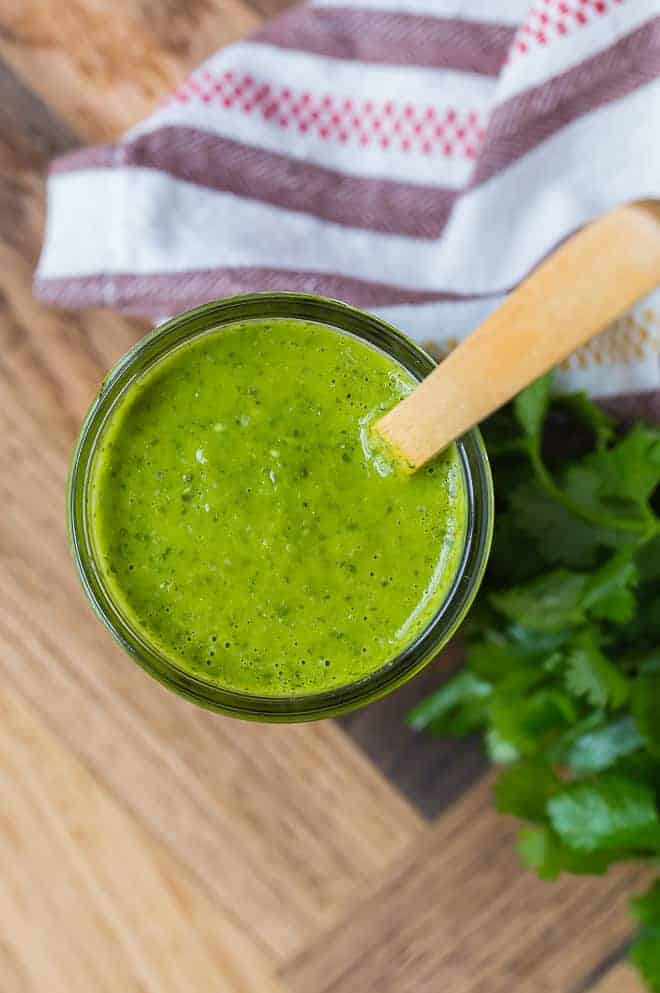 Image of a jar of freshly homemade salsa verde, shot from above. A wooden spoon is in the jar as well. 