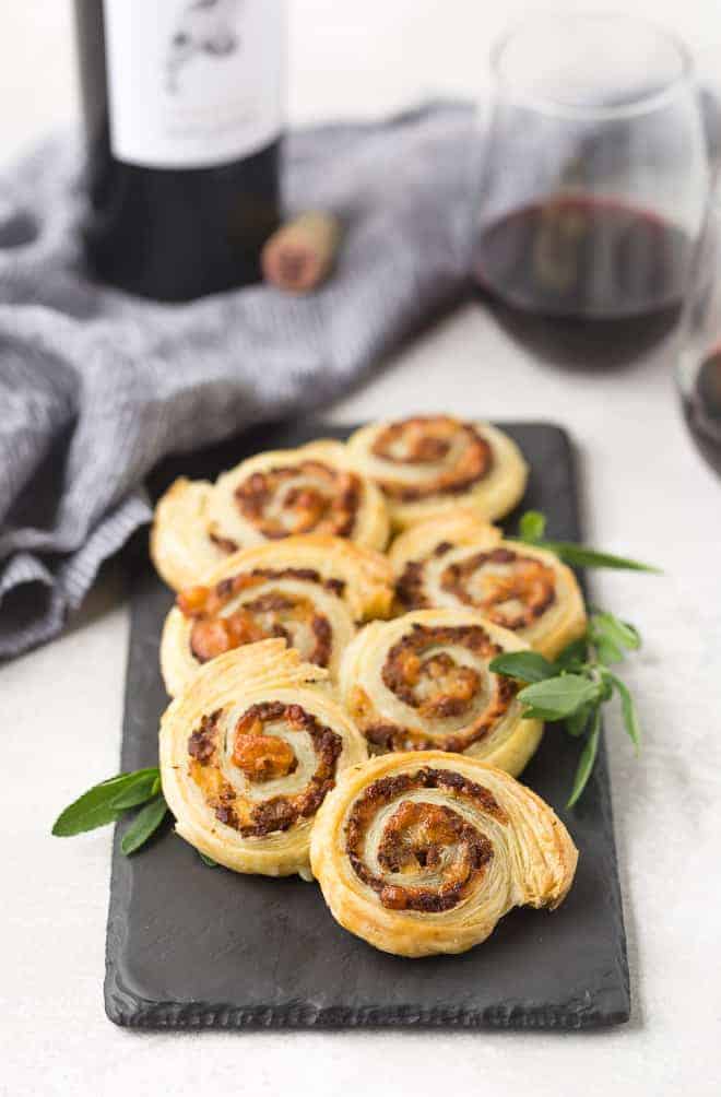 Puff pastry pinwheels on a slate board with fresh sage. Red wine in background.