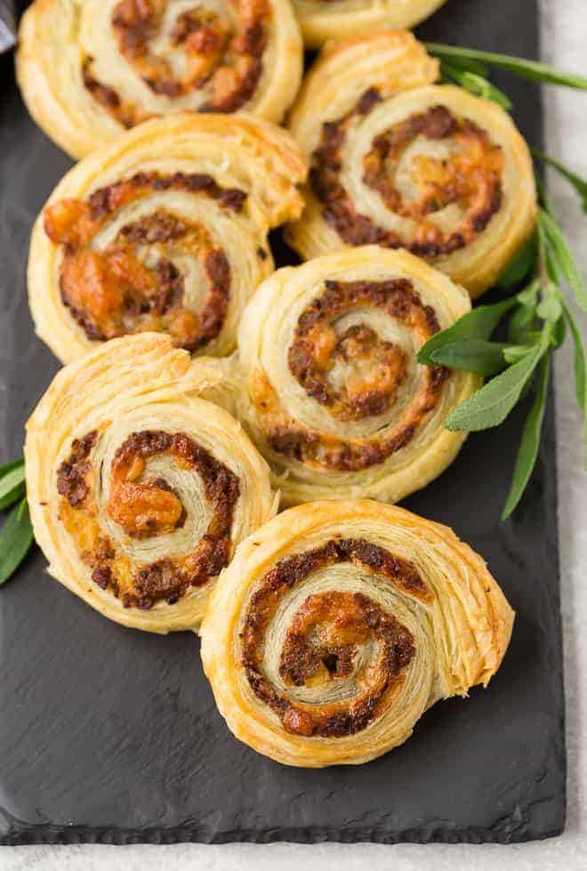 Pinwheels made with puff pastry, sausage, apple, cheese, and sage. Arranged on black slate.