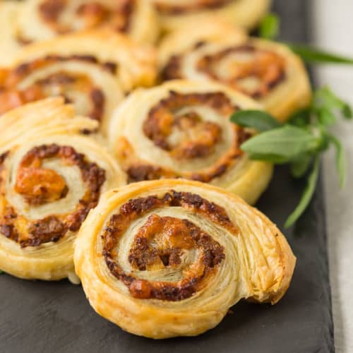 Pinwheel appetizers made with sausage and apple on a black slate board.
