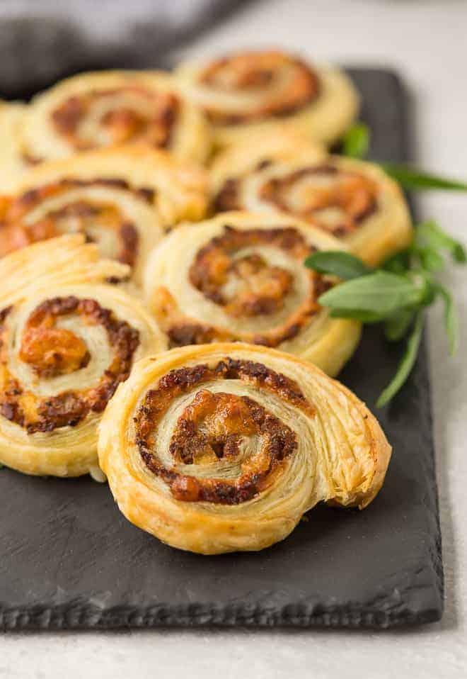 Pinwheel appetizers made with sausage and apple on a black slate board.