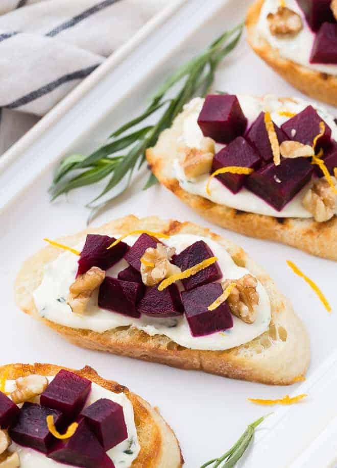Image of roasted beets on top of bruschetta toasts, garnished with orange and tarragon.