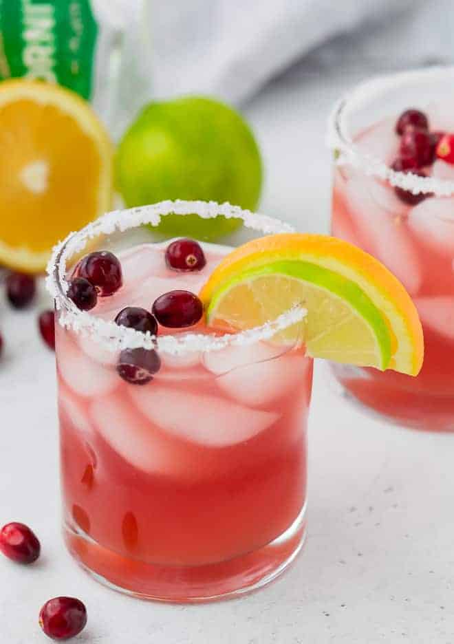 Image of a beautiful cranberry margarita in a salt rimmed glass, garnished with a lime wedge, an orange wedge, and fresh cranberries.
