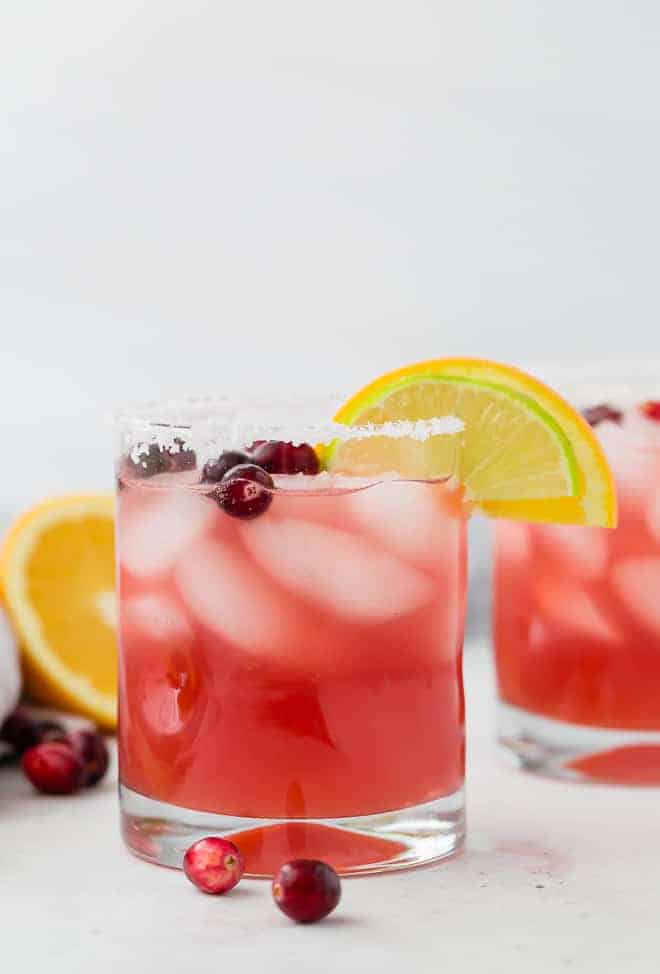 image of a cranberry margarita with orange and lime, garnished with fresh cranberries.