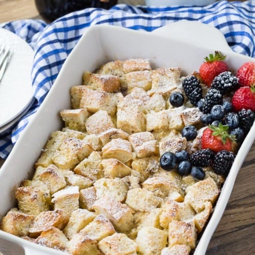 Overnight french toast casserole in a square baking dish, topped with powdered sugar and fresh berries.