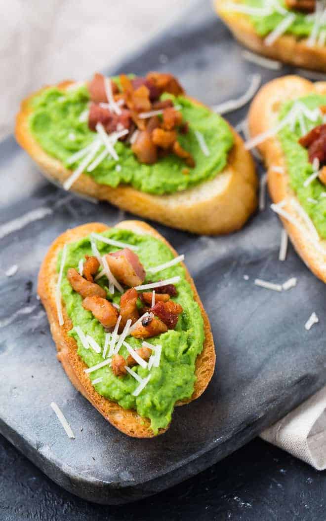 Image of pea crostini on a black marble serving platter, topped with pancetta and parmesan.