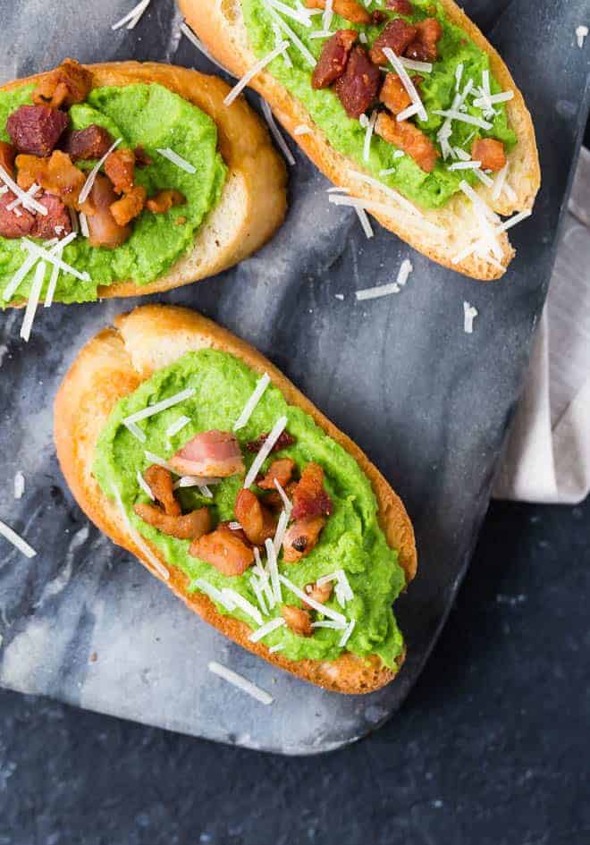 Image of creamy pea puree crostini, topped with crispy pancetta and vibrant white parmesan cheese.