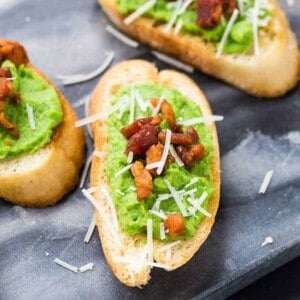 Image of creamy pea puree spread on crispy bread slices, topped with pancetta and parmesan.