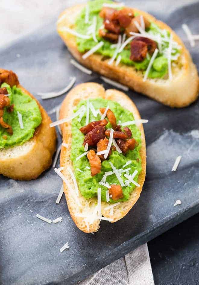 Image of creamy pea puree spread on crispy bread slices, topped with pancetta and parmesan.
