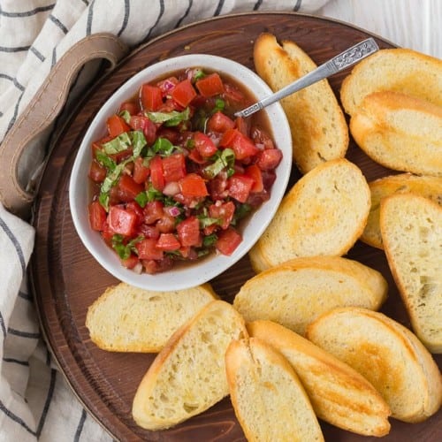 Image of the best tomato bruschetta recipe in a bowl served with crostini.