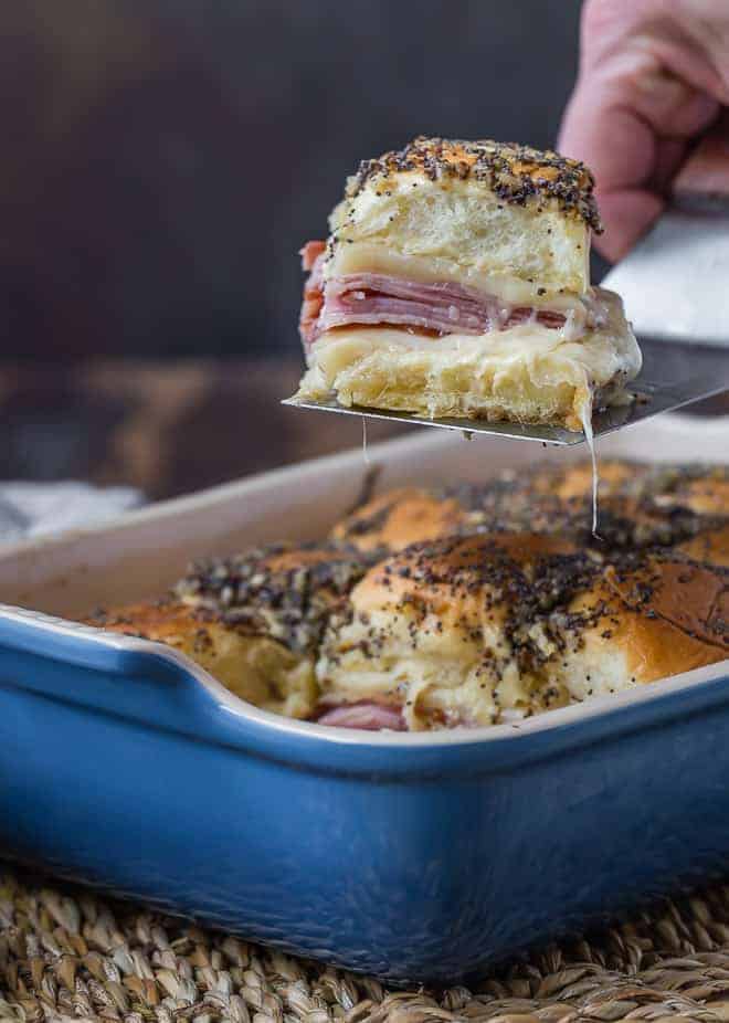 Image of a ham and cheese slider on a spatula. Topped with poppy seeds.
