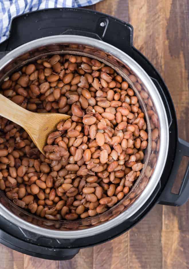 Image of cooked pinto beans in an instant pot with a wooden spoon on a wooden background.