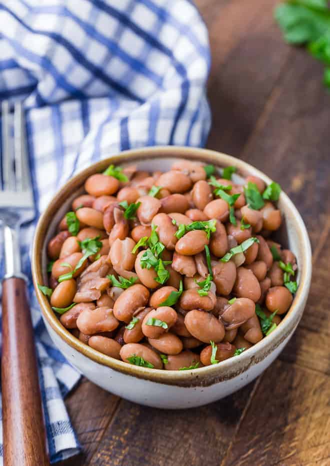 Image of Instant Pot pinto beans in a small bowl garnished with cilantro. A blue and white checkered cloth is in the background.