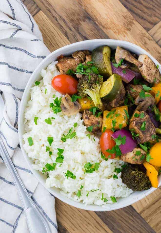 Image of sheet pan honey balsamic chicken and vegetables (tomatoes, peppers, broccoli, onions, mushrooms), served with rice and garnished with parsley.