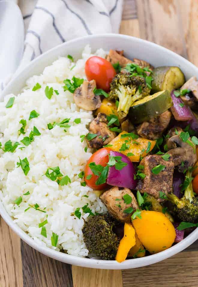 Image of a bowl of rice, chicken, mushrooms, peppers, onions, zucchini, broccoli, and tomatoes. This meal is garnished with fresh parsley.