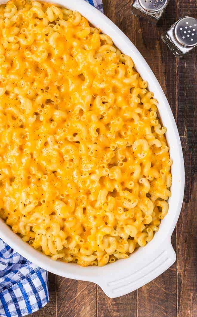 The best baked macaroni and cheese in an oval white casserole dish, overhead view on a wooden background.