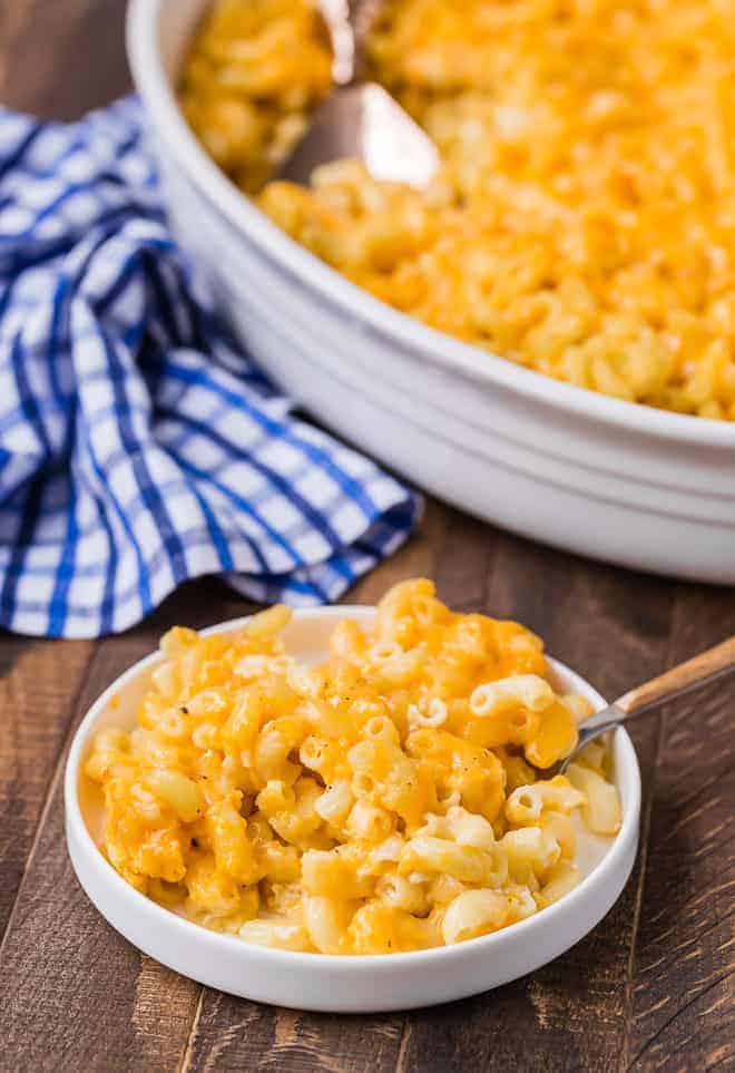 Macaroni and cheese on a plate with a fork. A casserole dish of macaroni and cheese is placed in the background.