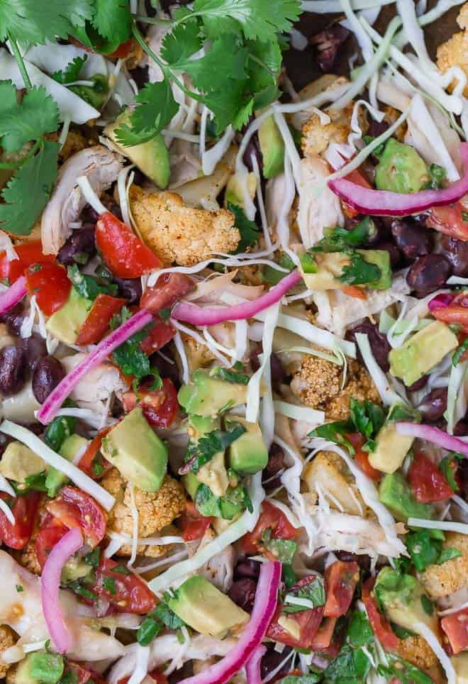 Image of roasted cauliflower topped with an assortment of southwestern flavors: pickled red onions, tomatoes, cabbage, avocado, black beans, and shredded cheese. 