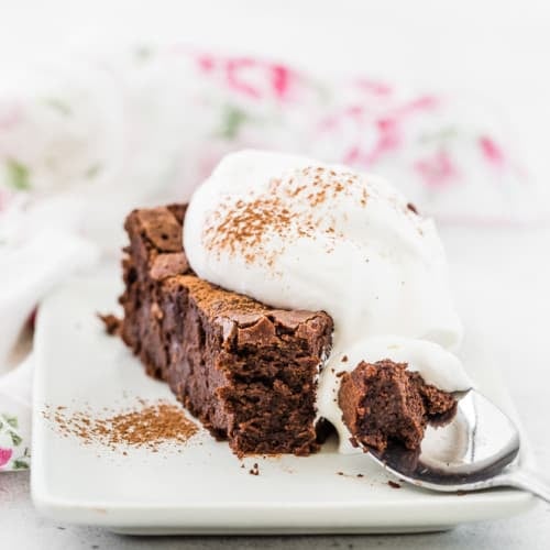 Image of flourless chocolate cake, spiced with chipotle chile, with a spoonful of whipped cream. One bite is taken from the end of the slice of cake and is pictured on a spoon.