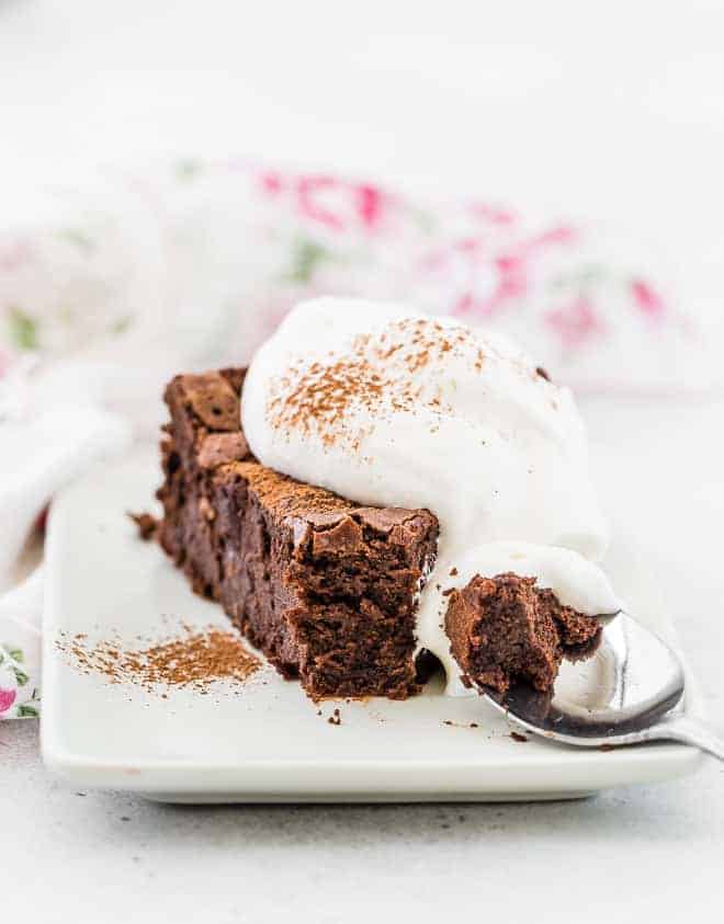 Image of flourless chocolate cake, spiced with chipotle chile, with a spoonful of whipped cream. One bite is taken from the end of the slice of cake and is pictured on a spoon.