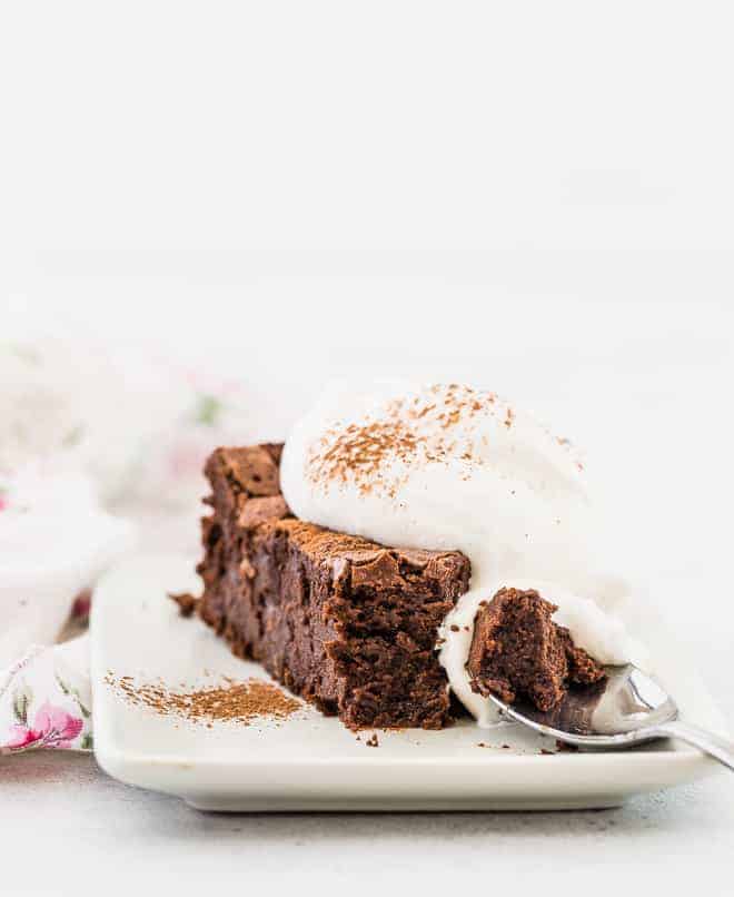 Image of decadent chocolate cake on a white plate with a spoon taking a piece out of it.