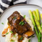 Image of a cooked short rib and gravy atop a pile of creamy mashed potatoes.