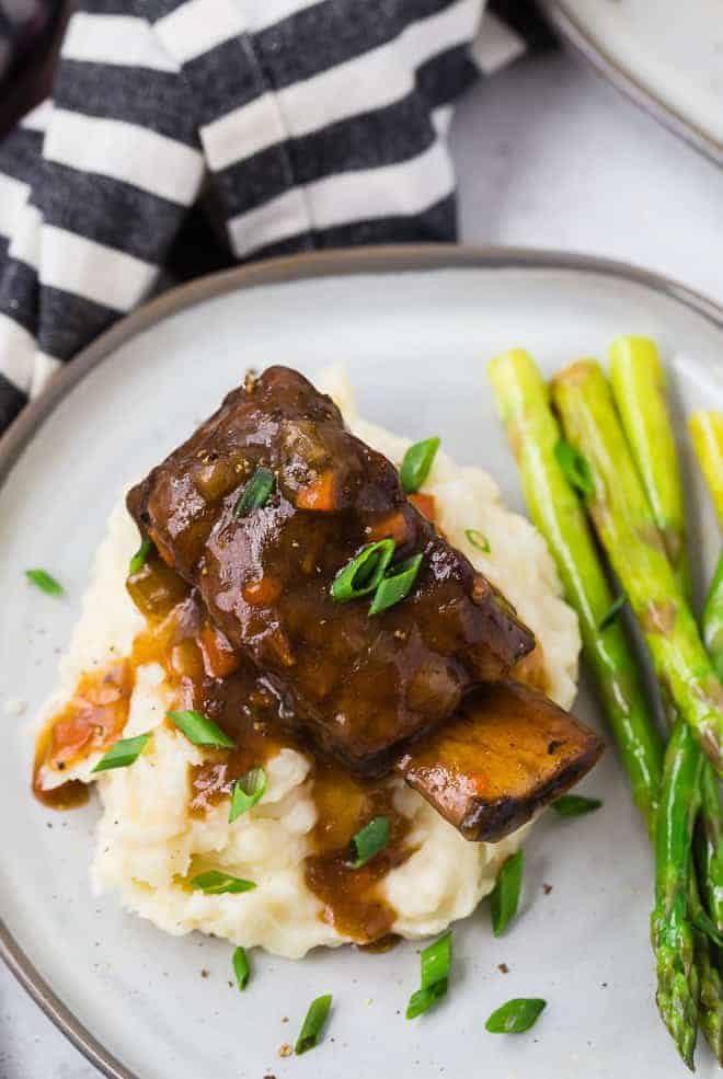 Image of a cooked short rib and gravy atop a pile of creamy mashed potatoes.