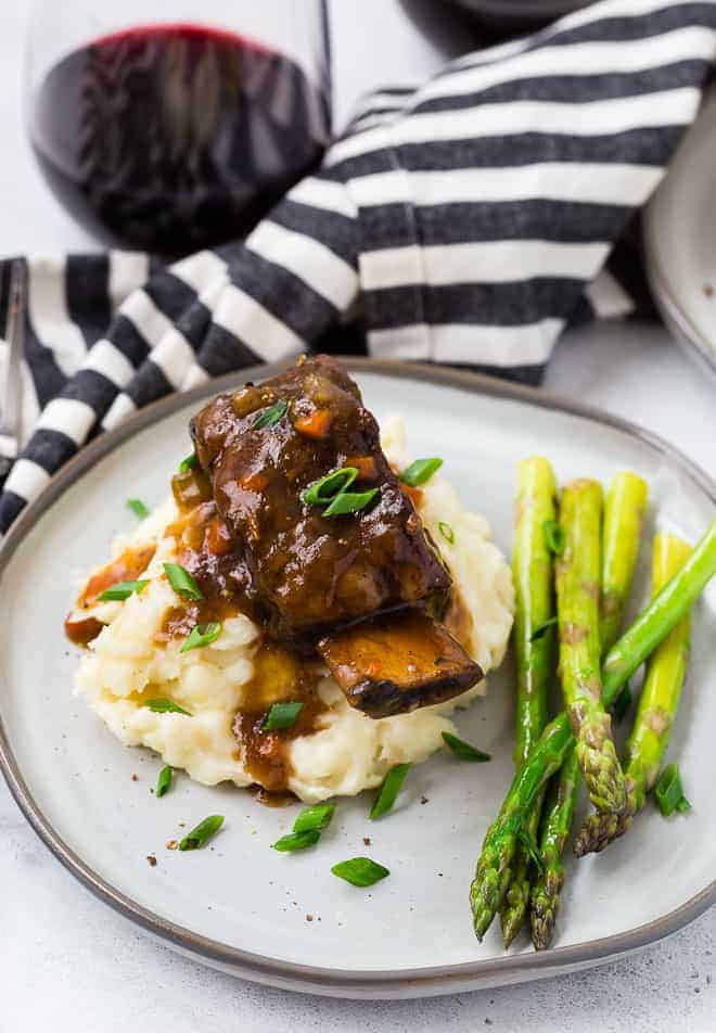 Image of short ribs cooked in an instant pot pressure cooker. Asparagus, mashed potatoes, and red wine are also pictured. 